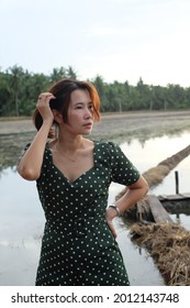 Asian Woman In Green Dress Poses Behind Is A Garden Ditch With Only Water.