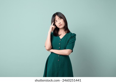 Asian woman with green suit is pondering against a green background. - Powered by Shutterstock