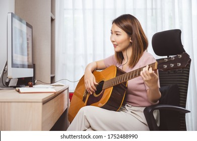 Asian Woman Guitar Player And Vlogger Playing Guitar In Front Computer At Home While Social Distancing Of Coronavirus Outbreak, Online Guitar Lesson,livestream On Social Media Concept.