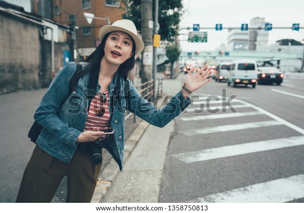 Asian woman with hand up calling taxi cab on osaka\
street. chinese girl traveler using cellphone app technology for\
passenger to request ride online. female holding mobile phone\
hailing uber car.