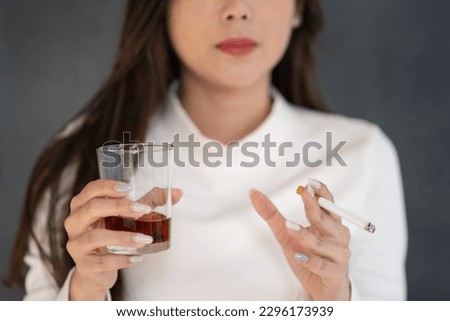 Asian woman hand drinking glass of alcohol and smoking cigarette.