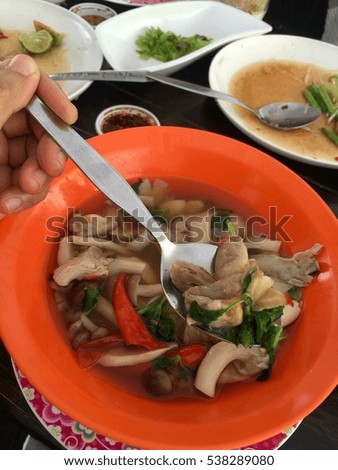 Asian woman hand hold stainless spoon with Thai healthy three kind of mushrooms spicy soup in orange bowl on food table at restaurant