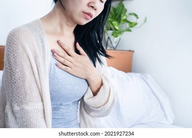 Asian Woman Hand Holding Chest Pain, Difficulty To Breathe, Heartburn From Acid Reflux After Wake Up In Bed  