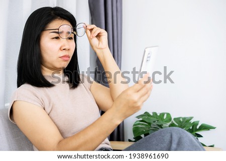 Asian woman hand holding  eyeglasses having problem with farsighted trying to read text on smart phone with eye sight blurred vision  
