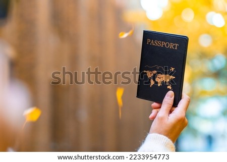 Asian woman hand holding passport on beautiful yellow ginkgo leaves falling in autumn with sunlight shining in the morning. People enjoy outdoor lifestyle travel Japan on winter holiday vacation.