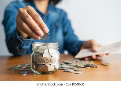 asian woman hand is putting a coin in a glass  bottle and a pile of coins on a brown wooden table,Investment business, retirement, finance and saving money for future concept.