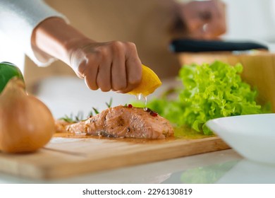 Asian woman hand squeezing lemon juice on piece of seafood salmon steak during cooking meal in the kitchen at home. Attractive girl enjoy eating healthy food and salad for dinner. - Powered by Shutterstock