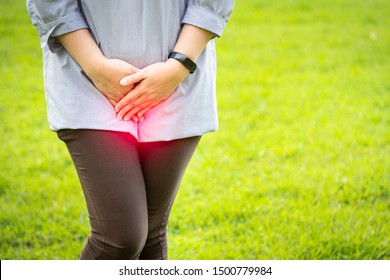 Asian woman with hands holding pressing crotch lower abdomen,female patient having painful suffering from stomachache in green background at outdoor park,urinary tract Infection,cystitis concept