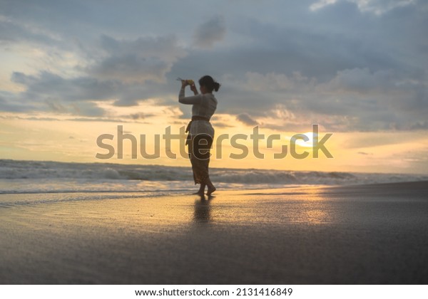 Asian woman with hands praying on\
the seashore during Melasti ceremony before Nyepi day. Holidays,\
festivals, rituals, arts, culture of the Indonesian\
people.