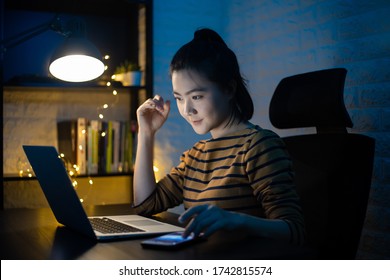 Asian woman happy smiling working on a laptop at the night at home. WFH. Work from home avoid COVID 19 concept.