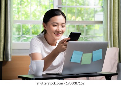 Asian Woman Happy Typing Message With Smart Phone Sitting On The Bed At Home. WFH. Work From Home. Social Distancing Concept.