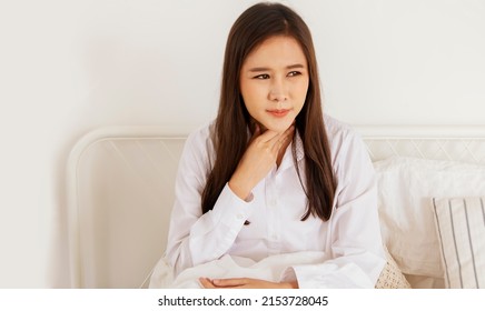Asian woman has a sore throat, dry throat with mucus in her throat while waking up in bed in the morning : Young woman's cold is caused by an infection in the respiratory tract.