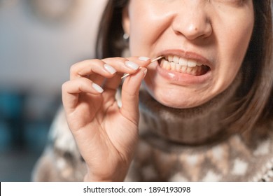 Asian woman has a toothache after a big meal and she pulls out the remains of food from the cavity in her teeth with a toothpick. The concept of dental health and cleaning