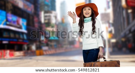 Asian woman with hat holding luggage against blurry new york street