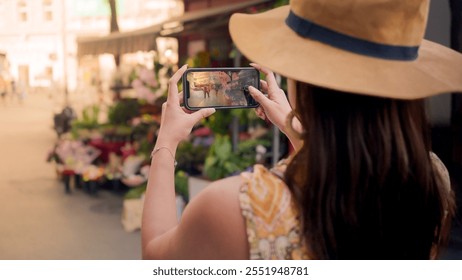 An Asian woman in a hat taking a photo of a flower market in Budapest with a smartphone, capturing urban street life and vibrant colors. - Powered by Shutterstock