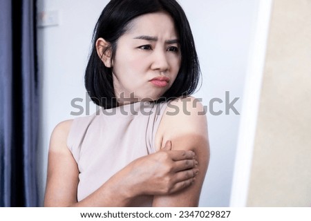 Asian woman have problem with uneven tan on arms checking on dark, sunburn and damaged skin in front of a mirror 