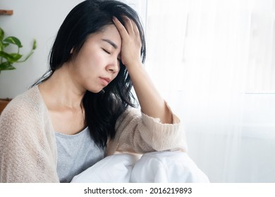 Asiatische Frau mit Kopfschmerzen Migräne, Kater, Schlafmangel im Bett nach dem Aufwachen morgens  