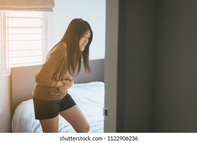 Asian woman having painful stomachache and gastritis in bedroom after wake up,Hands touching her stomach - Shutterstock ID 1122906236