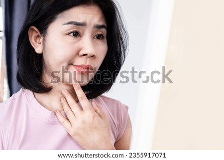 Asian woman having problem with Bell's Palsy,Facial Palsy, hand holding her face in front of a mirror 
