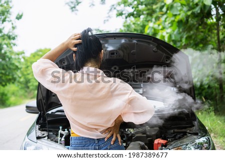 Asian woman having problem with broken, overheat car while driving alone on the road standing with smoke from the engine 