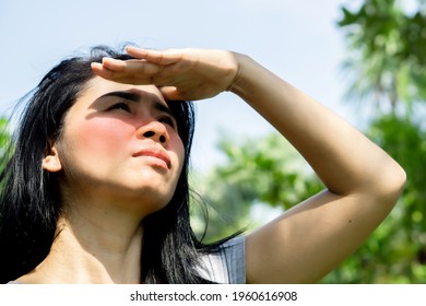 Asian woman having problem sunburn redness on face skin hand cover her face to protect ultraviolet from sunlight standing outdoors under sunny 