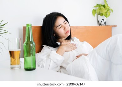 Asian Woman Having Problems With GERD , Acid Reflux, And Heartburn With Gastritis From Drinking Beer Before Sleeping In Bed 