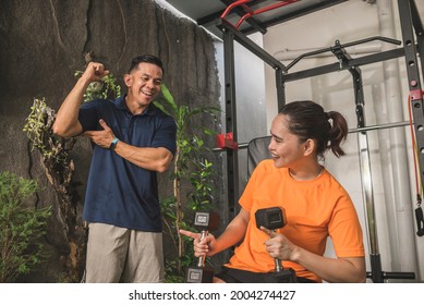 An asian woman and her personal fitness trainer share a lighthearted moment in between workout sets. Casual scene at the home gym. - Shutterstock ID 2004274427