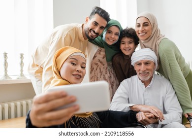 asian woman in hijab taking selfie with multiethnic muslim family on mobile phone