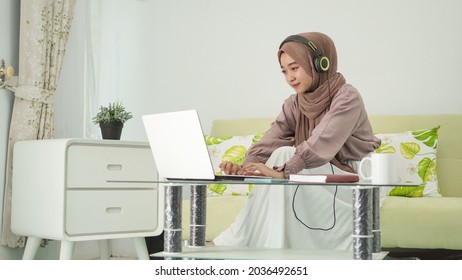 Asian Woman In Hijab Working From Home Typing Laptop While Listening