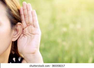 Asian woman hold her hand near her ear and listening in green field