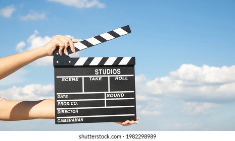 Asian woman holding clapper board with blue sky grass field, open landscape view. Hands holding film slate cinema clapper on spring background. Film making video shooting production outdoors footage - Shutterstock ID 1982298989
