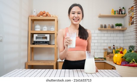 Asian Woman Holding And Drinking Fresh Milk From Glass. Healthy Diet After Exercise In Kitchen, Sport, Health ,exercising, Lifestyle, Healthy Concept.Smiling Thai Female  Happy After Yoga Class.