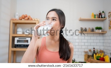 Asian Woman holding and drinking fresh milk from glass. healthy diet after exercise in kitchen, sport, health ,exercising, lifestyle, Healthy concept.Smiling Thai female  happy after yoga class.