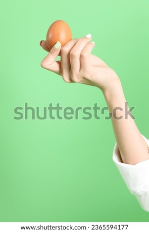 The Asian woman holding egg in the hand on the green background.
