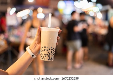 Asian woman holding the famous taiwanese bubble milk tea at night marketplace
