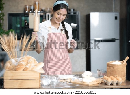 Asian woman holding flour rolling pin prepare to thresh flour making homemade pizza on wooden table in kitchen. Young female chef kneading yeast dough with hand to bake delicious bread or bakery.