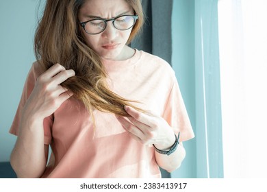 Asian woman holding her damaged split ended hair. Hair damage is risk for further damage and breakage. It may also look dull or frizzy and be difficult to manage.