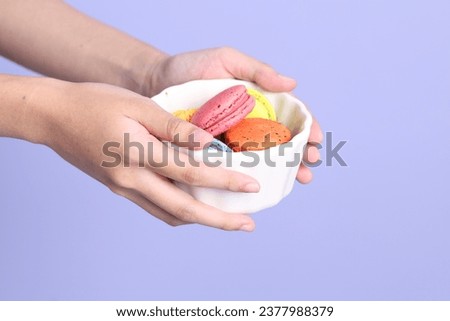 The Asian woman holding macaroon on the purple background.