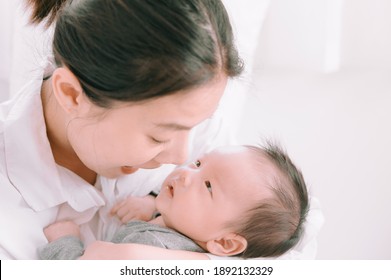 Asian Woman Holding A Newborn Baby In Her Arms At Home.Mother Day And Newborn Baby Infant Health Care Concept.