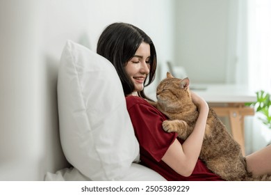 Asian woman holding and play with little cat with happiness at home. Attractive beautiful female lying down on bed, spend leisure time hug and massaging her pet animal with gentle in bedroom in house. - Powered by Shutterstock