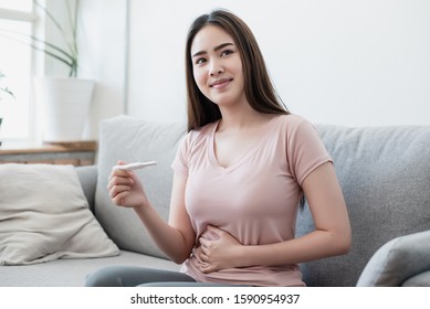 Asian Woman Holding The Pregnancy Test And She Is Pregnant. She Is Happy With Beaming Face.