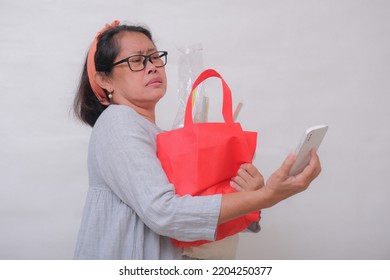 An Asian woman holding shopping bags has difficulty looking at her cell phone.