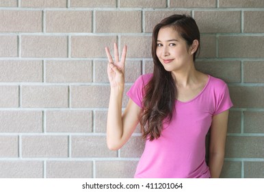 Asian Woman Holds Up Three Fingers Motion On Blurred Bricks Wall Background