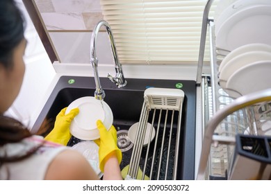 Asian woman housewife wearing gloves washing dishes in the kitchen sink