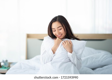 Asian woman hug the pillow in the bed smile and happy - Powered by Shutterstock