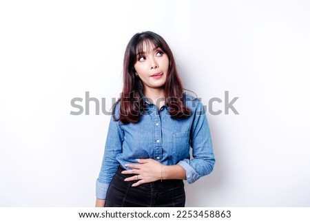 An Asian woman is hungry and touching her belly while looking aside thinking what to eat