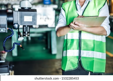 Asian Woman Is Industrial Engineer Or Qc Team Holding Th Clipboard While Standing In The Heavy Duty Manufacturing Shop Floor. Factory Worker Concept.