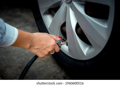 Asian woman inflates tires at a gas station, looking at the dial of the auto inflator to check the pressure level. Beautiful lady inflating tires with automatic inflator outside, self service