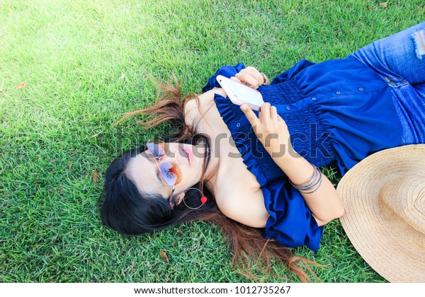 Asian  woman  laying  and play phone on green grass\
at public park