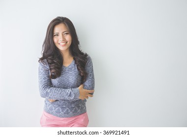 Asian woman leaning on a white wall. Casual woman crossed arm smiling looking happy in grey sweater - Shutterstock ID 369921491